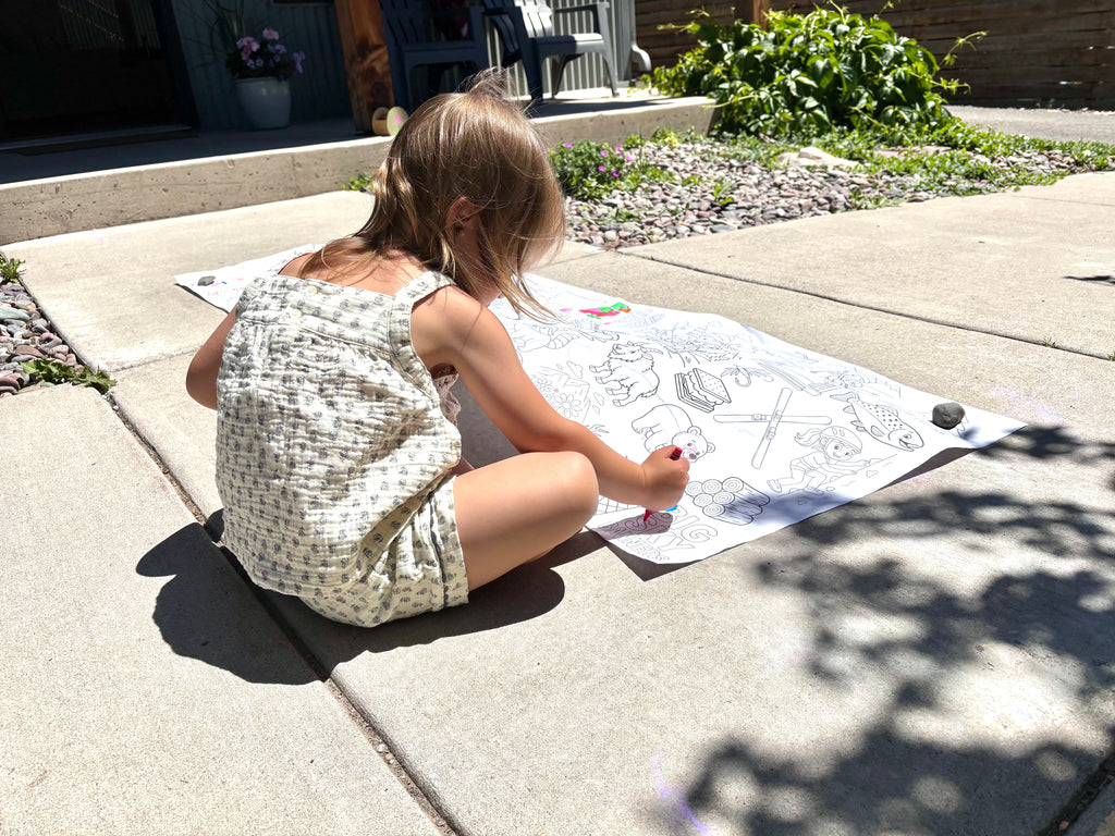 Child coloring on a large sheet of paper outdoors